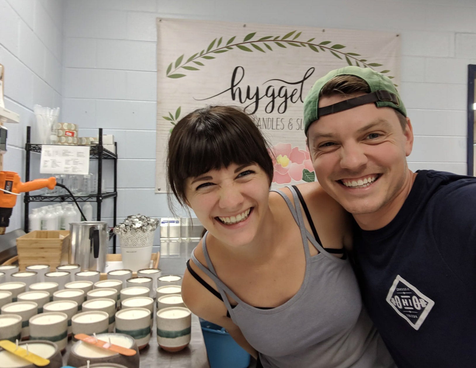 Two people smiling in front of a display of candles with a 'hygge' sign in the background.