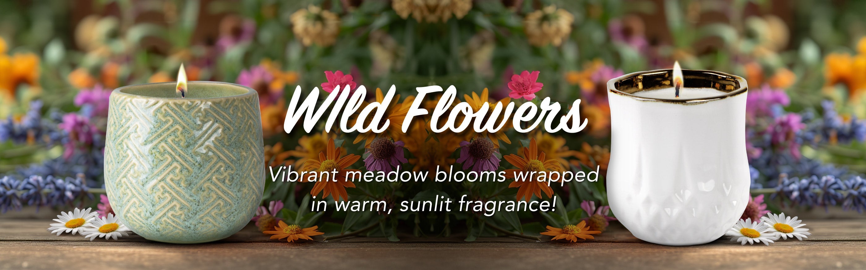Two candles with 'Wild Flowers' branding on a wooden surface with flowers in the background.